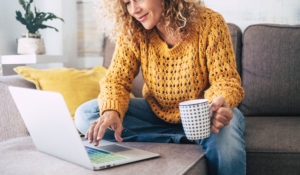 Woman sitting on couch drinking coffee using a laptop