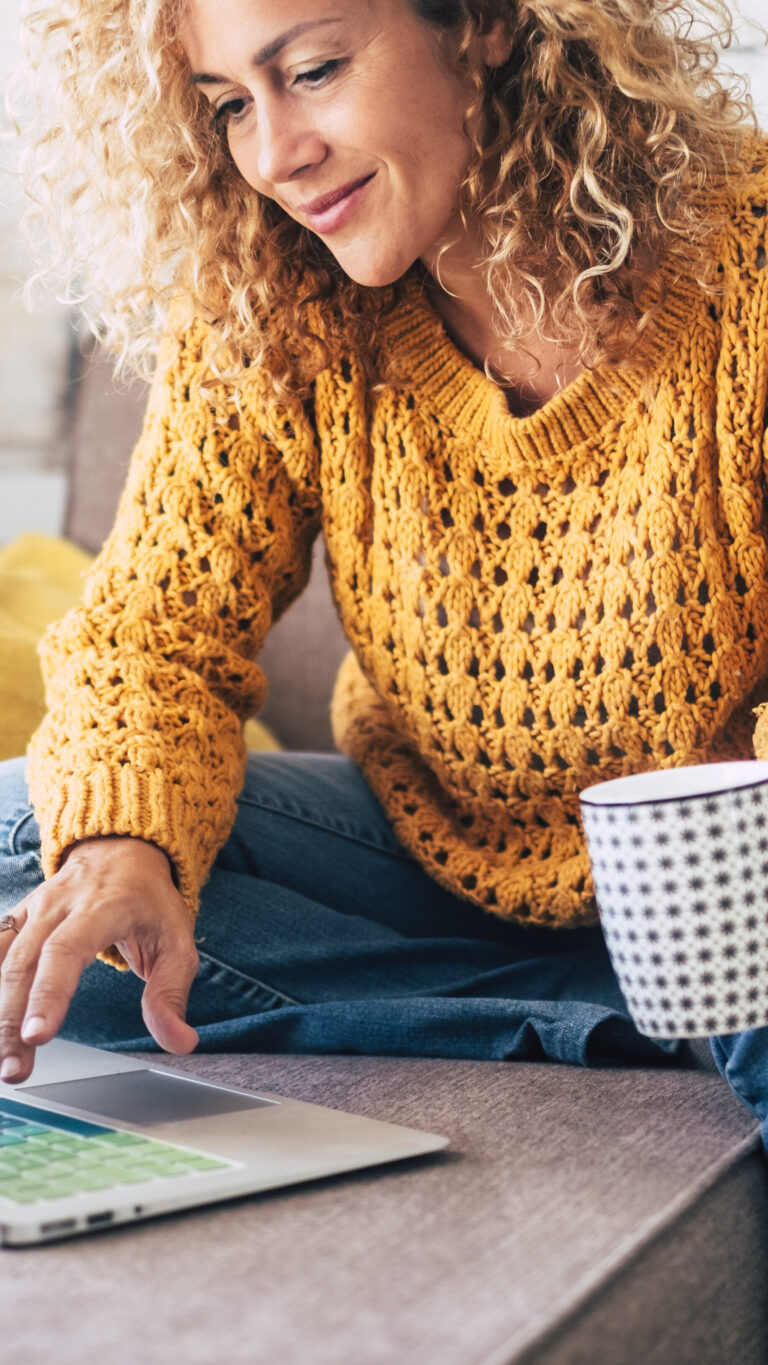 Woman sitting on couch drinking coffee using a laptop