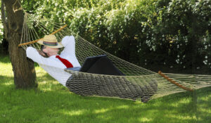 happy man relaxing in a backyard hammock with laptop computer