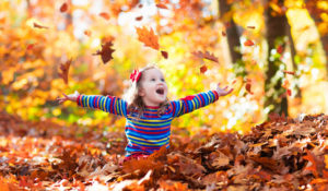 happy girl playing in fallen leaves