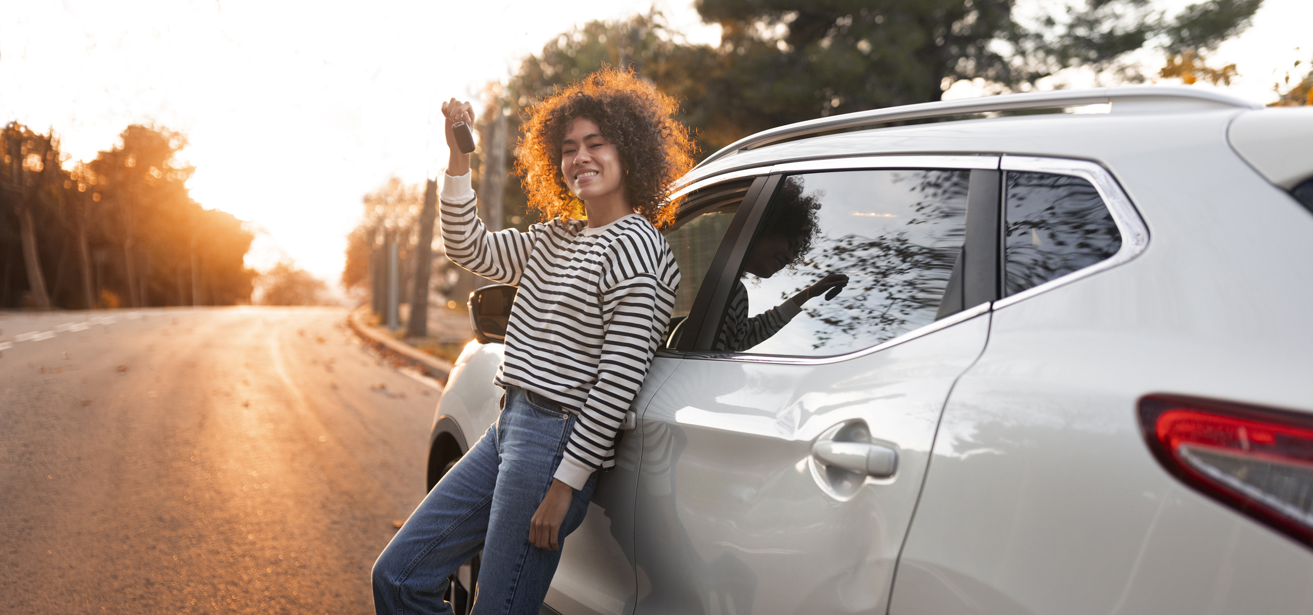 young person with new car shows off keys on scenic road at dusk