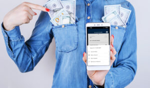 woman with shirt pockets full of US dollars, shows phone screen for Skip-A-Payment service